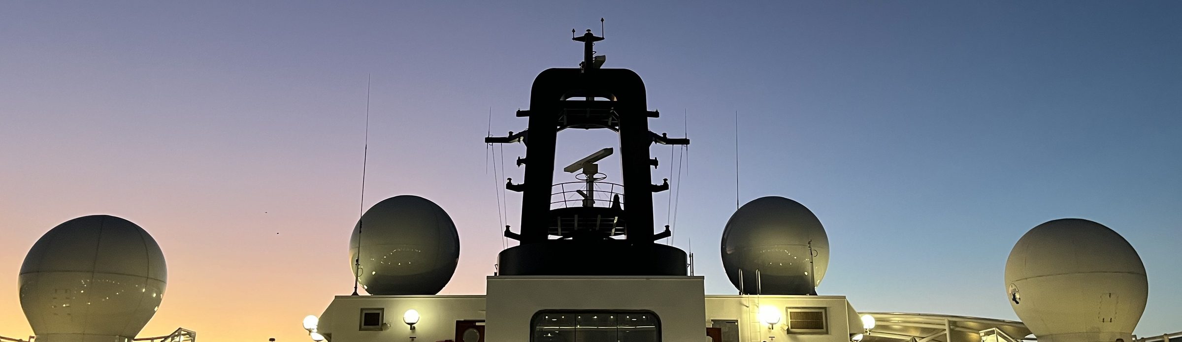 Radarkuppeln und Mast auf der Brücke eines Schiffs in der Dämmerung