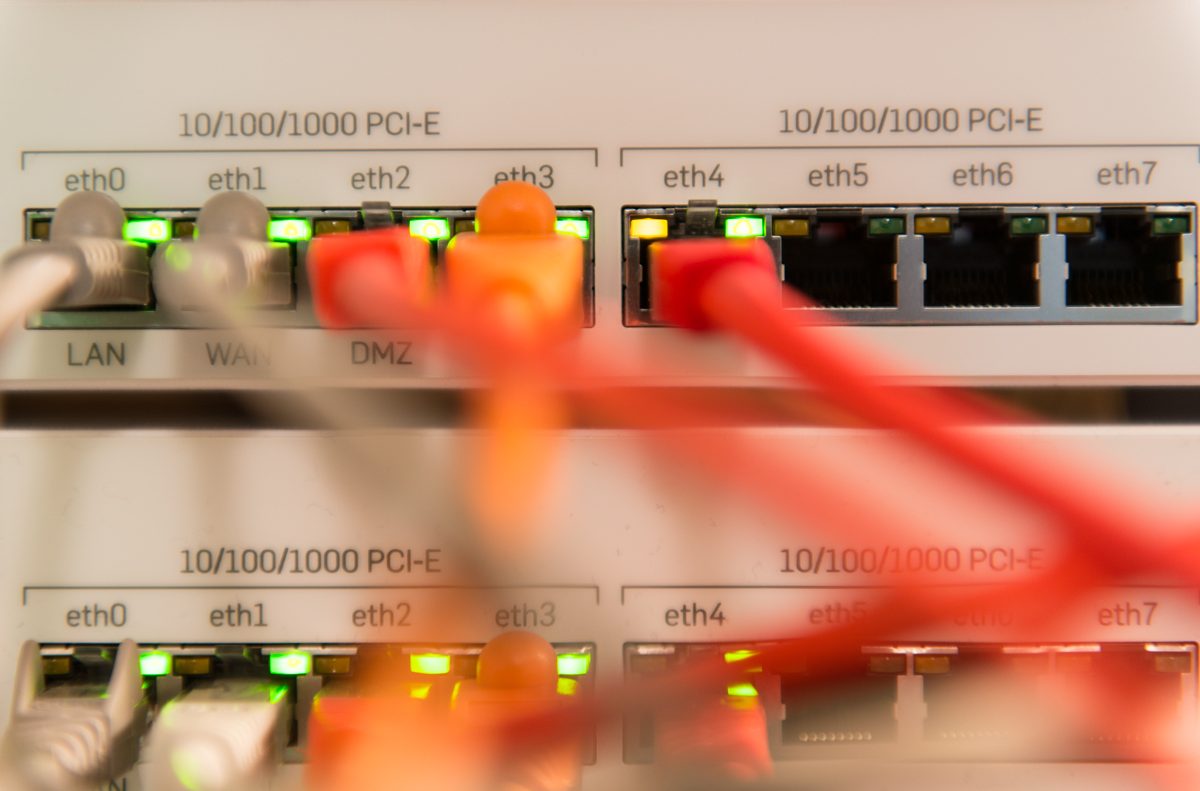 Netzwerkanschlüsse einer Firewall mit leuchtenden Statuslampen und roten Patchkabeln