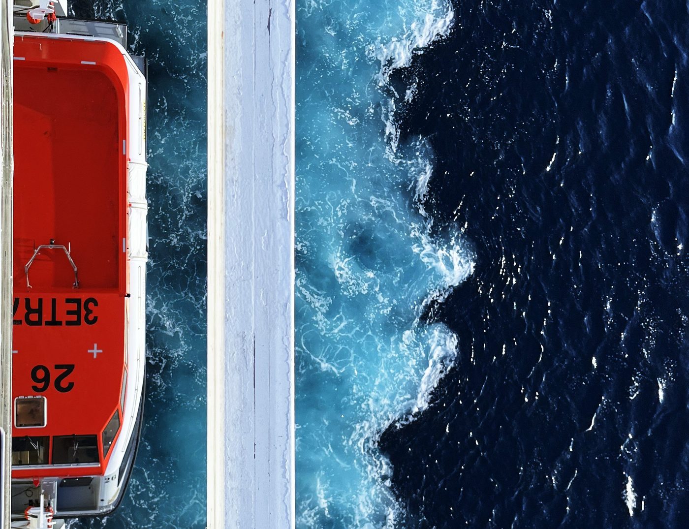 Orangefarbenes Rettungsboot an der Bordwand über dem schäumenden Kielwasser
